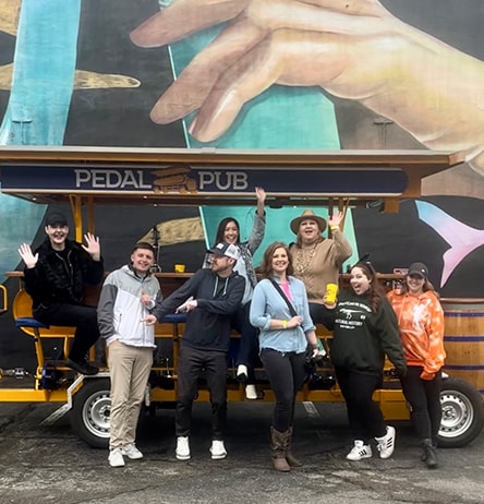 group of friends smiling in front of pedal pub bike