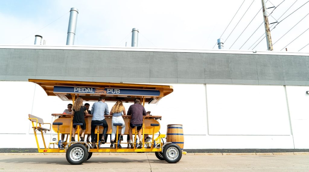 riders aboard pedal pub bike in front of a plain building