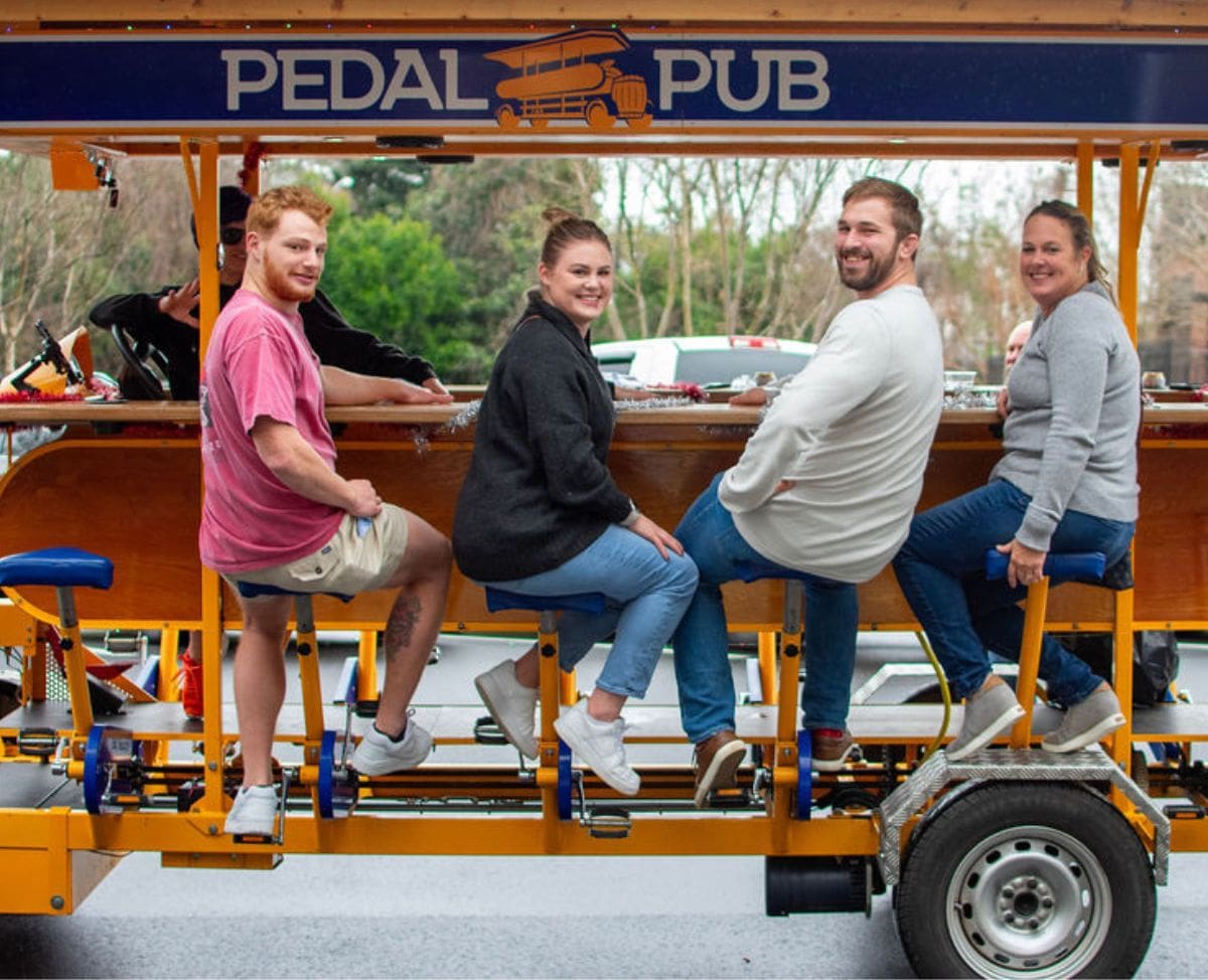 group of friends smiling on the pedal pub bike