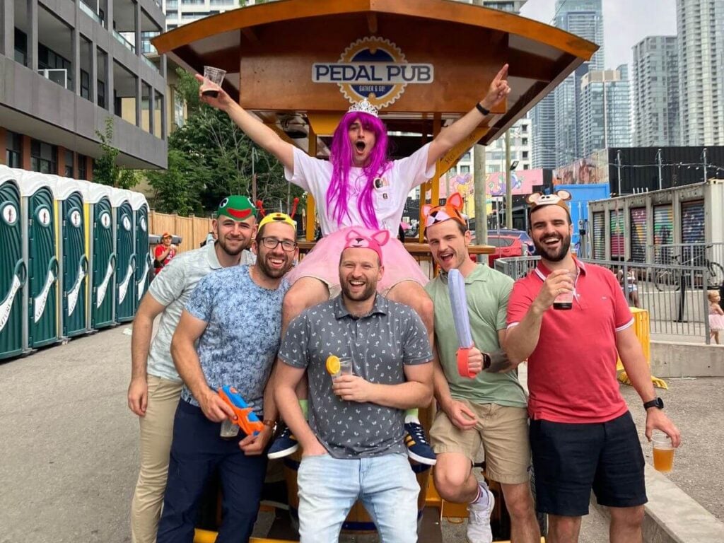 Private group tour on a Pedal Pub bike in Toronto's King Street Village, guests posing and smiling on a sunny summer day