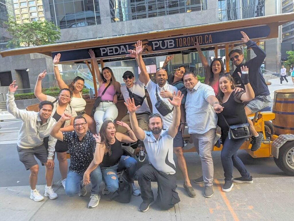 Energetic mixed group on a private Pedal Pub Toronto tour posing on King Street with the city skyline in the background