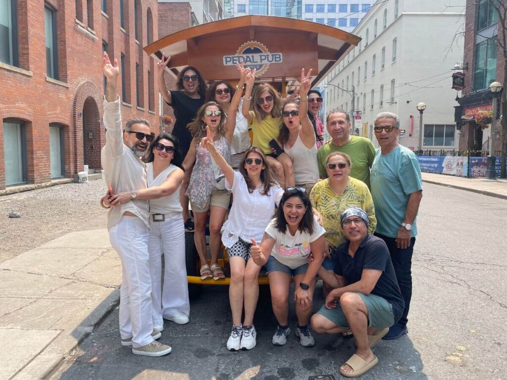 Large group celebrating a private event on a Pedal Pub Toronto tour in the Entertainment District, guests stacked on and around the bike