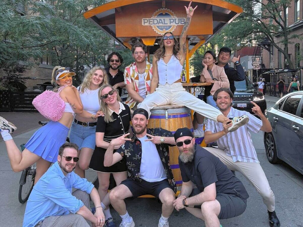 Large group of women on a private Pedal Pub Toronto tour posing in the Distillery District alley with the CN Tower visible in the background