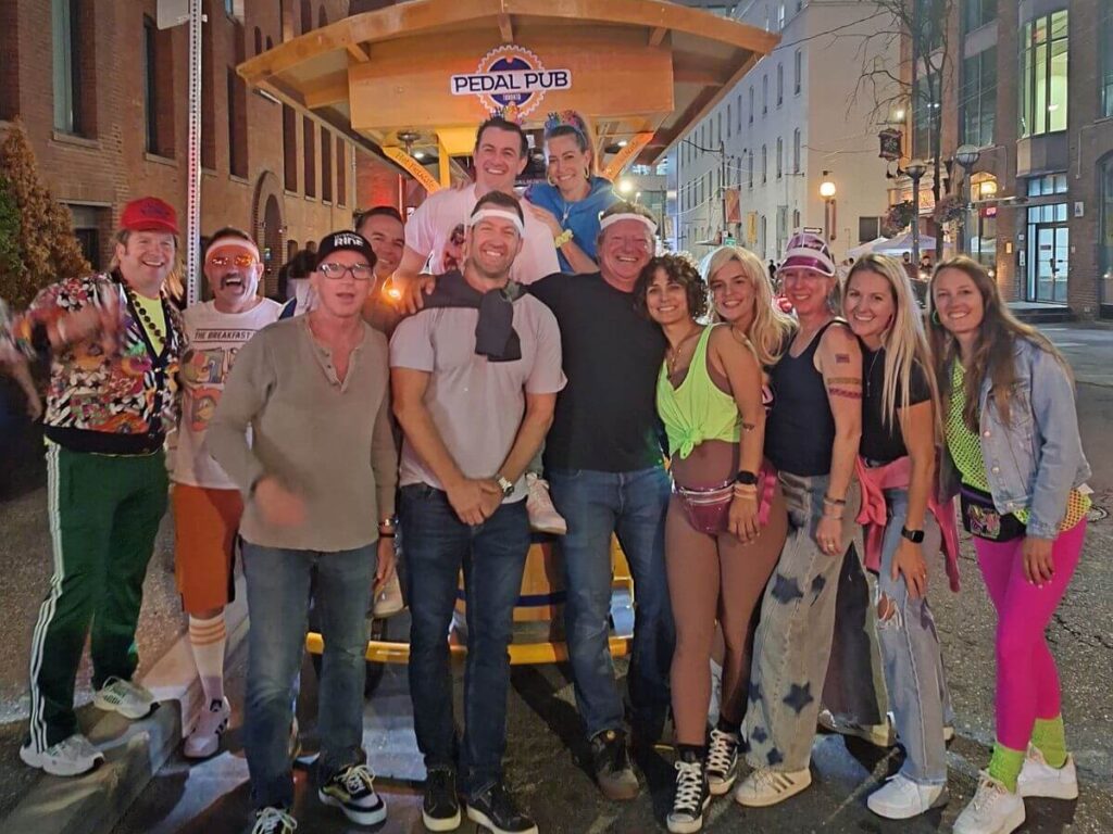 Birthday group wearing matching blue "Birthday Crew" t-shirts on a private Pedal Pub Toronto tour, posing with the CN Tower in the background