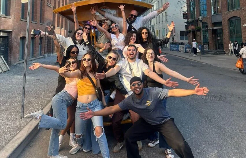 Group of friends posing for a picture together in front of the Pedal Pub bike downtown