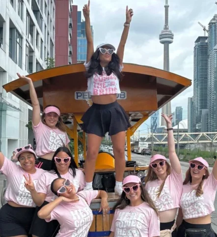 Bride and friends in matching pink shirts celebrating on a Pedal Pub Toronto bachelorette party in downtown Toronto