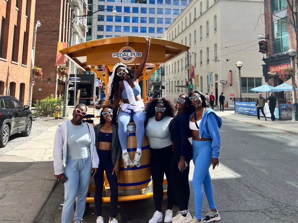 Bride in blue with friends posing on a Pedal Pub Toronto bachelorette party with the CN Tower behind them