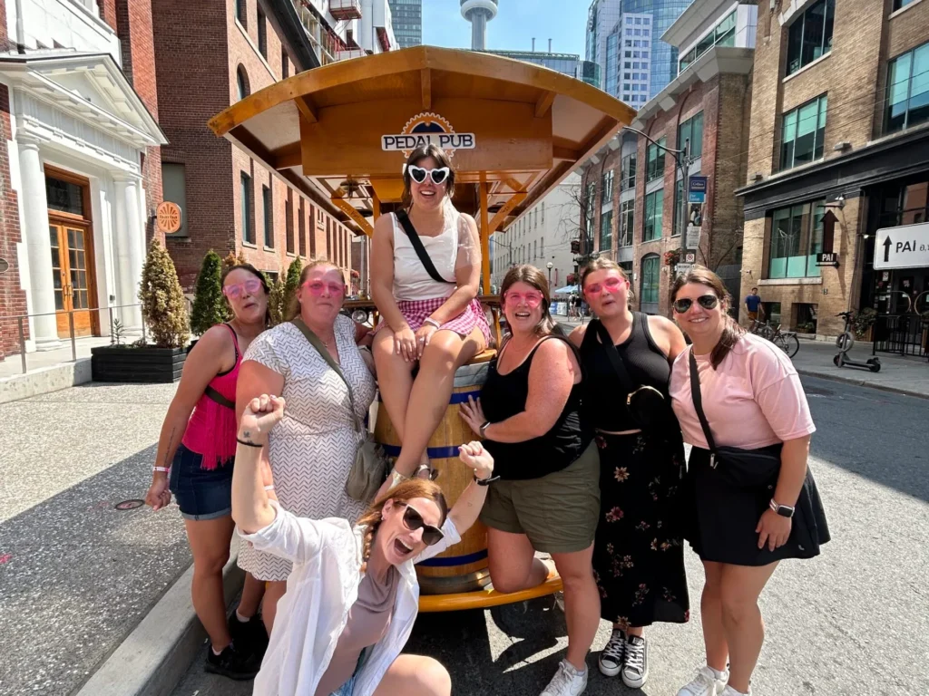Women posing around a Pedal Pub Toronto party bike during a summer bachelorette outing in downtown Toronto
