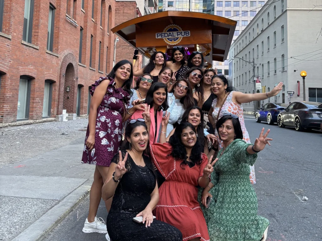 Group of women posing on a Pedal Pub Toronto party bike in downtown Toronto with the CN Tower behind them